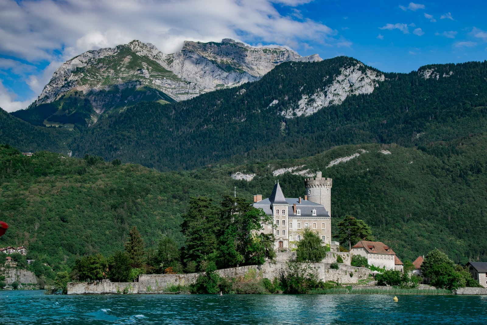 Le lac d'Annecy et le château de Duingt au pied des montagnes boisées, sous un ciel bleu d'été